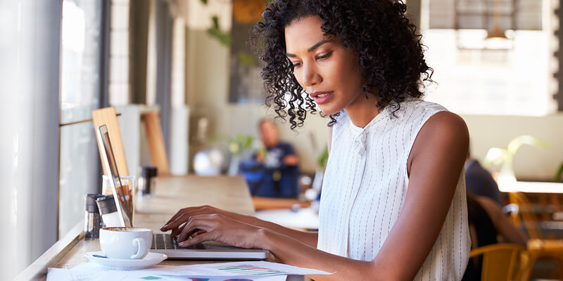 curly woman typing on her laptop with a cup of coffee next to her