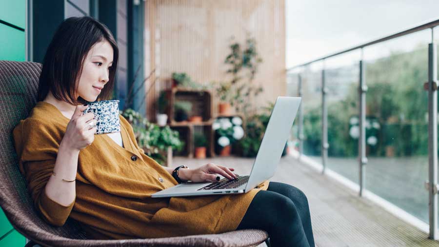 a woman having a laptop in a balcony doing her work while drinking coffee