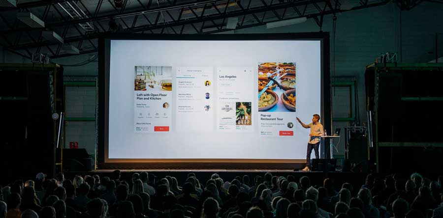 a group of crowded people watching virtual event presentation on stage